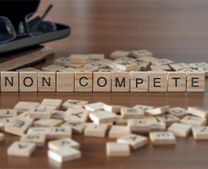 Non compete word or concept represented by wooden letter tiles on a wooden table with glasses and a book